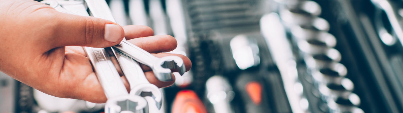 Hand holding a wrench with tools in the background